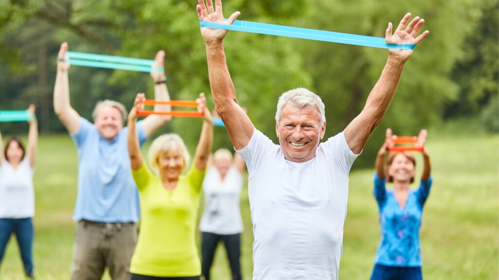 Group of older adults exercising outdoors with resistance bands.