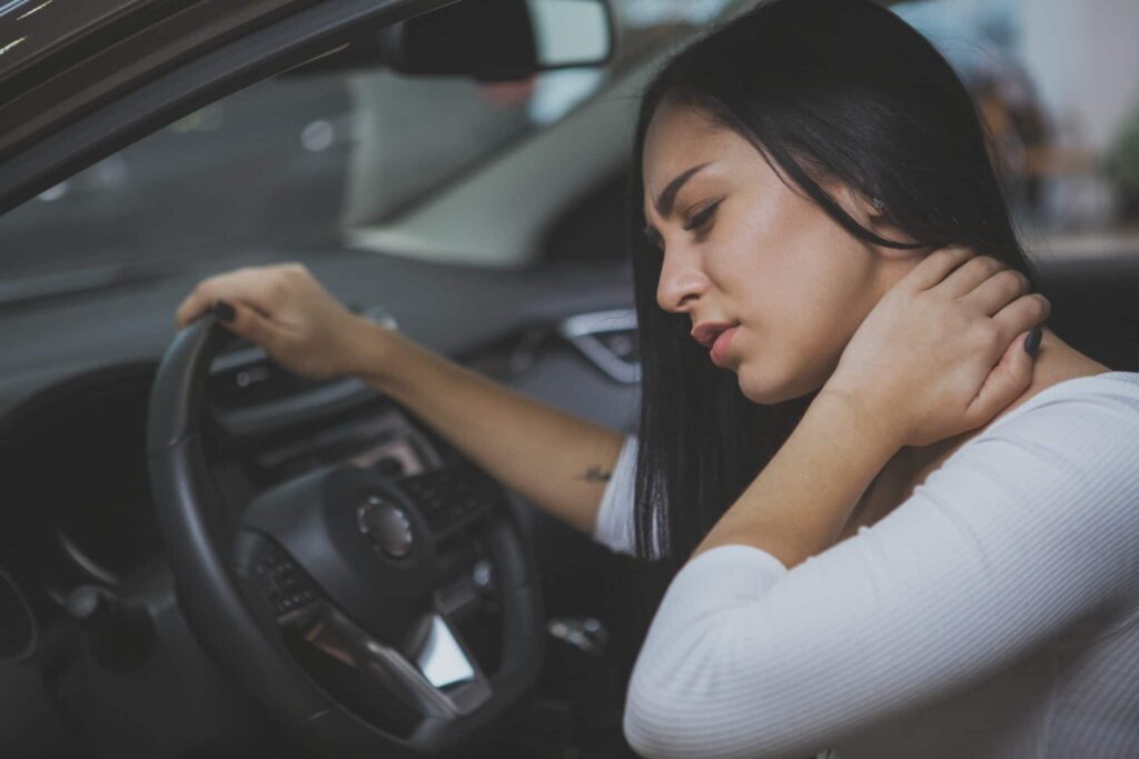 Woman in a car holding her neck in pain after a strain or injury.