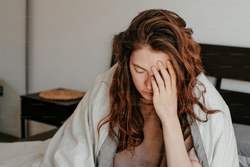 Woman sitting on a bed with her hand on her face, showing fatigue or discomfort.
